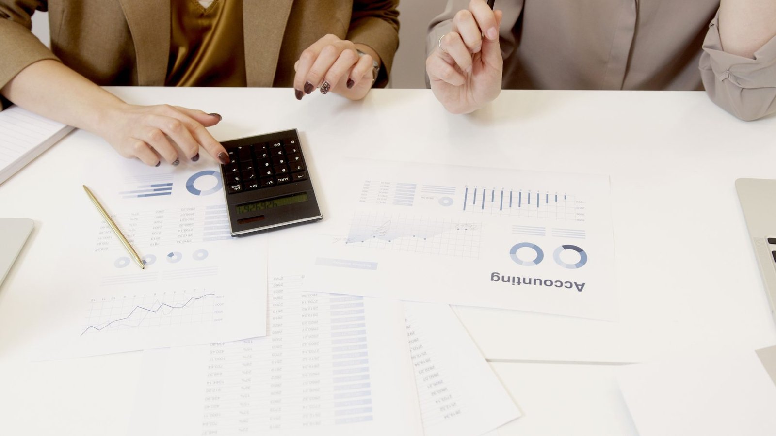 Two people reviewing printed accounting reports and charts with a calculator